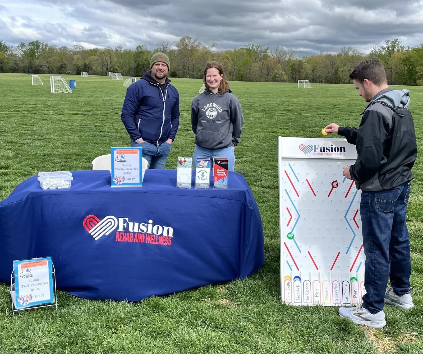 People gather beside a Fusion outreach table with a Spectrum Sea Turtles sign at an outdoor event.
