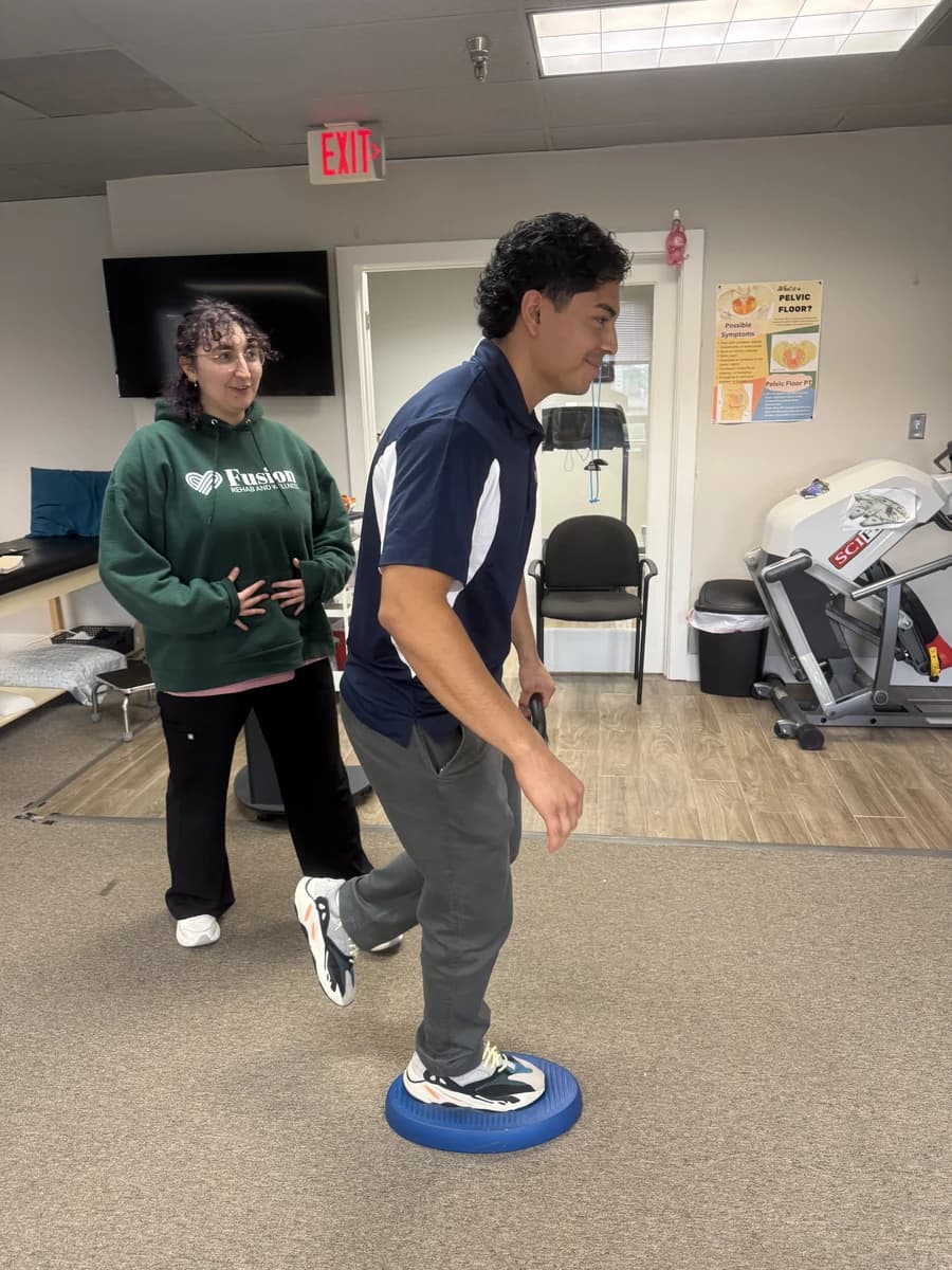 A Fusion team member demonstrates single-leg balance on a blue balance cushion.
